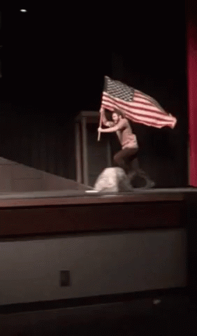 A Person Holding An American Flag On A Stage In A Dark Room GIF