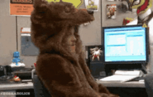 A Person In A Bear Costume Is Sitting At A Desk In Front Of A Computer GIF
