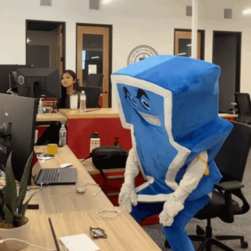 A Person In A Blue And White Costume Is Sitting At A Desk With A Laptop GIF