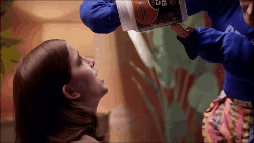 A Person In A Blue Shirt With The Letter D On It Is Pouring Something Into A Woman 'S Mouth GIF
