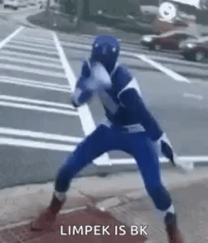 A Person In A Blue Superhero Costume Is Standing On A Sidewalk In A Parking Lot . GIF