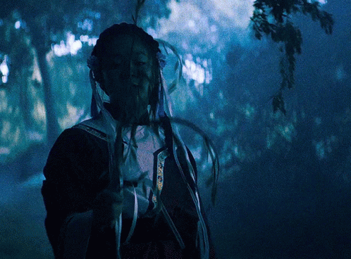 A Person In A Dark Forest Holding A Feather In Their Hand GIF