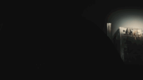 A Person In A Dark Room With A Light Shining On Their Face GIF