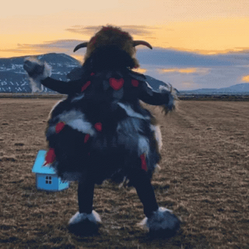 A Person In A Furry Costume Stands In A Field With A Small Blue House In The Background GIF