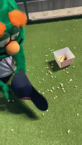 a person in a green costume is kicking a popcorn bucket on the grass .
