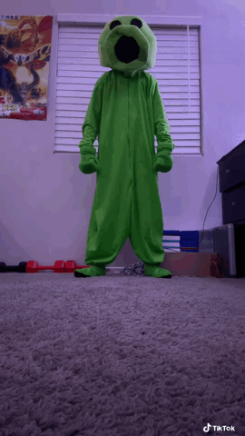 A Person In A Green Monster Costume Stands In Front Of A Window With A Poster On It GIF