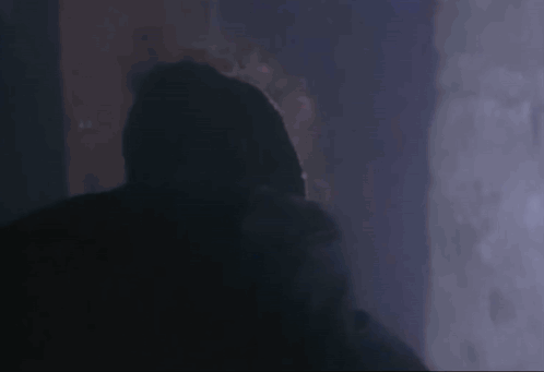 A Person In A Hooded Jacket Is Standing In The Dark . GIF