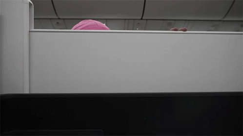 A Person In A Pink Hat Is Peeking Out From Behind A White Wall GIF