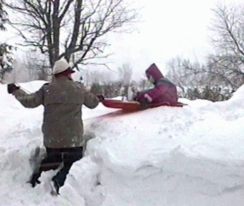 A Person In A Pink Hooded Jacket Is Sledding Down A Snow Covered Hill GIF