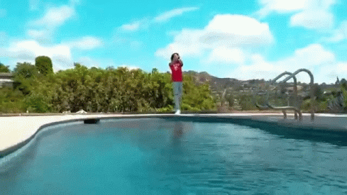A Person In A Red Shirt Is Standing On The Edge Of A Swimming Pool . GIF