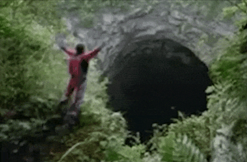 A Person In A Red Suit Is Standing In A Cave GIF
