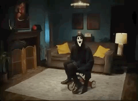 A Person In A Scary Mask Is Sitting On A Tricycle In A Living Room . GIF