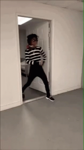 A Person In A Striped Shirt And Black Pants Stands In A Doorway GIF
