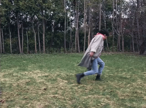 A Person In A Trench Coat Is Running In A Field GIF