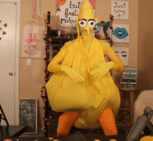 A Person In A Yellow Chicken Costume With A Sign That Says But First Make It GIF