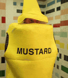 A Person In A Yellow Mustard Costume Is Standing In Front Of A Tiled Wall GIF