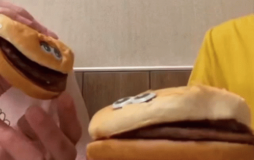 A Person In A Yellow Shirt Is Holding A Stuffed Hamburger With A Face On It GIF