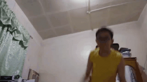 A Person In A Yellow Shirt Is Standing In A Room GIF
