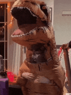A Person In An Inflatable Dinosaur Costume Is Standing In A Room GIF