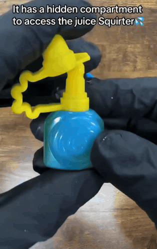 A Person In Black Gloves Is Holding A Juice Squirter That Has A Hidden Compartment To Access The Juice GIF