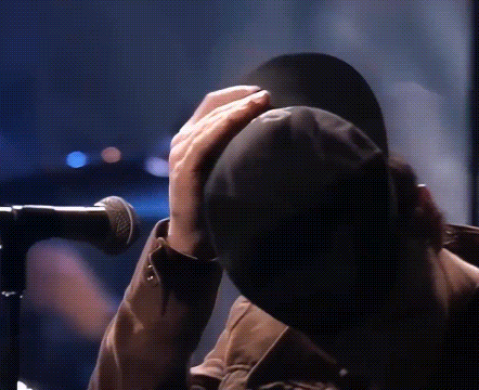a person is covering their face with a hat while standing in front of a microphone