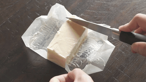 A Person Is Cutting A Piece Of Butter With A Knife On A Table GIF