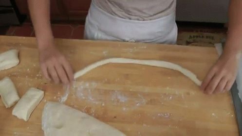 A Person Is Cutting A Piece Of Dough On A Wooden Table With An Apple Pie Box In The Background GIF