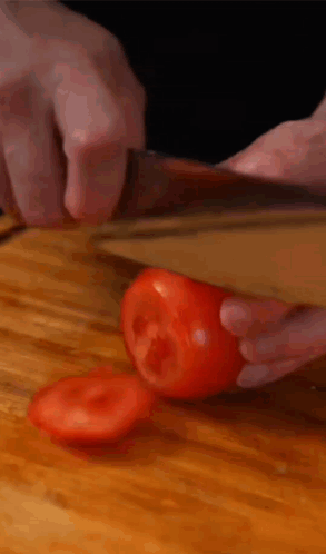 A Person Is Cutting A Tomato With A Knife On A Wooden Cutting Board GIF