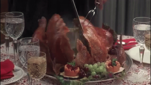 A Person Is Cutting A Turkey On A Table With Wine Glasses And Water GIF