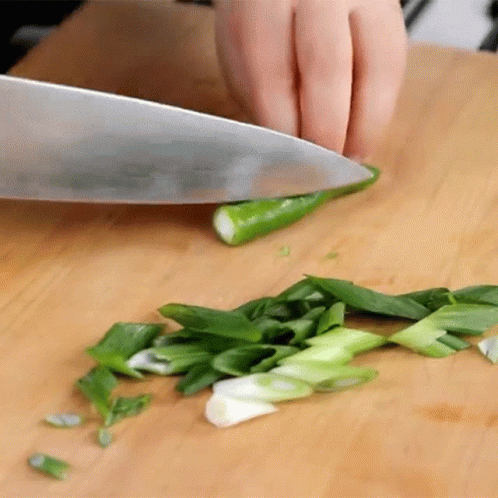 A Person Is Cutting Green Onions With A Knife On A Cutting Board GIF