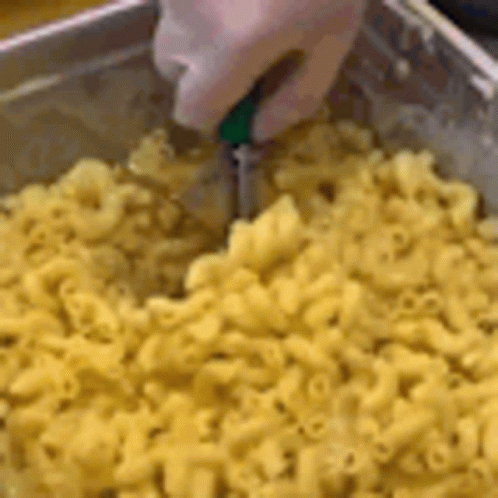 A Person Is Cutting Macaroni And Cheese With A Knife In A Pan . GIF
