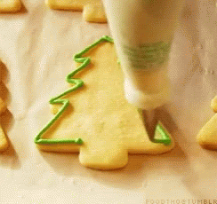 A Person Is Decorating A Cookie In The Shape Of A Christmas Tree With Green Frosting GIF