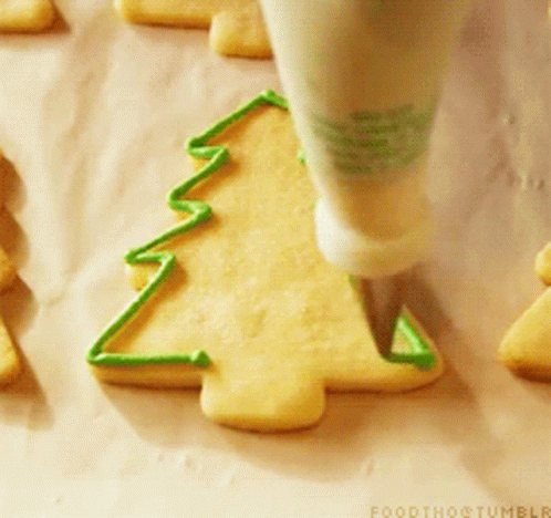 A Person Is Decorating A Cookie In The Shape Of A Christmas Tree With Green Frosting GIF
