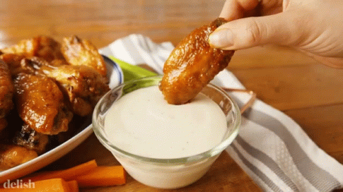 A Person Is Dipping A Chicken Wing Into A Bowl Of Ranch Dressing GIF