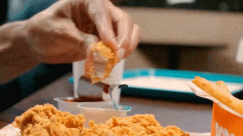 A Person Is Dipping A Piece Of Fried Chicken Into A Sauce GIF