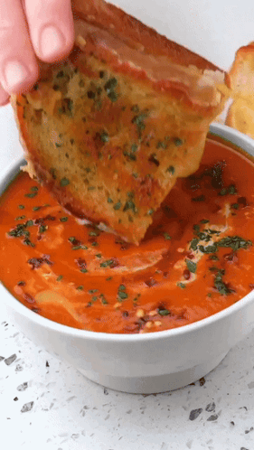 a person is dipping a piece of grilled cheese into a bowl of soup