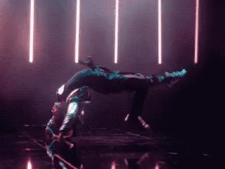 a person is doing a handstand in a dark room with lights behind them