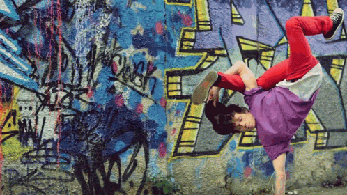 A Person Is Doing A Handstand In Front Of A Wall With Graffiti On It Including The Letter R GIF