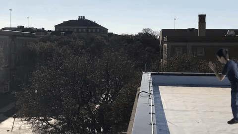 A Person Is Doing A Trick On A Rooftop With A Building In The Background GIF