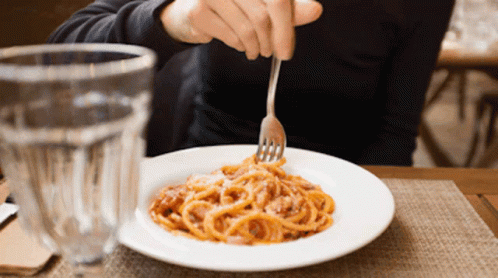 A Person Is Eating Spaghetti With A Fork In Front Of A Glass GIF