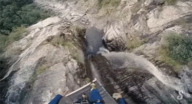 A Person Is Flying Over A Waterfall In The Mountains . GIF