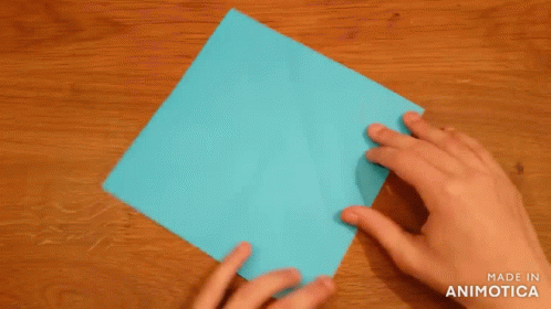 A Person Is Folding A Piece Of Blue Paper On A Wooden Table . GIF