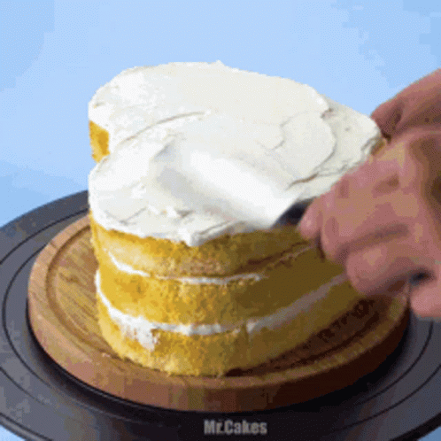A Person Is Frosting A Cake On A Wooden Cutting Board GIF