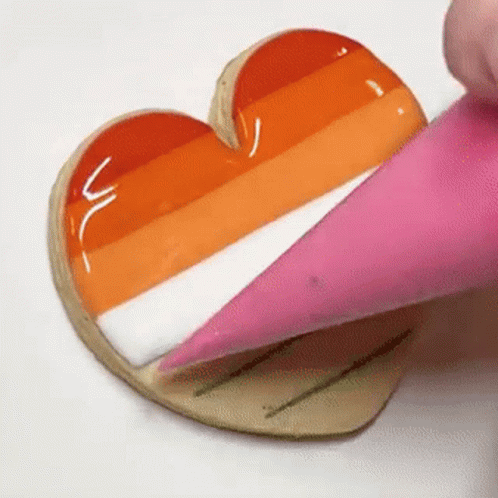 A Person Is Frosting A Cookie In The Shape Of A Heart With A Pink Frosting Cone . GIF