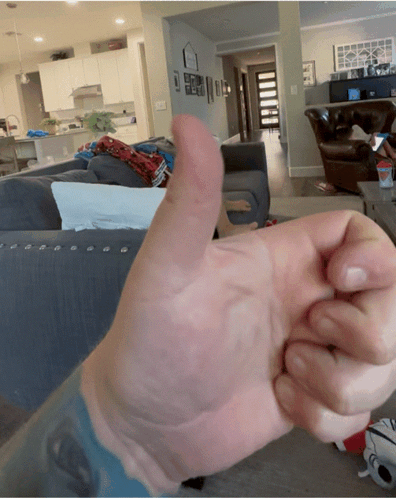 A Person Is Giving A Thumbs Up In Front Of A Living Room GIF