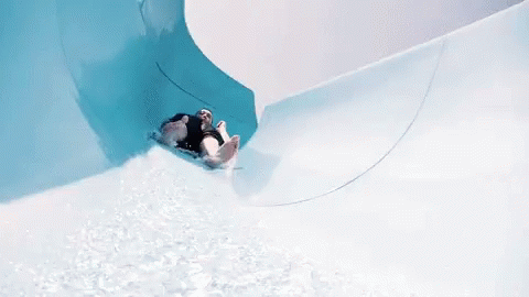 A Person Is Going Down A Water Slide In A Pool GIF