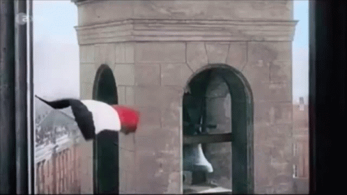 A Person Is Hanging From A Tower With A Flag On It GIF