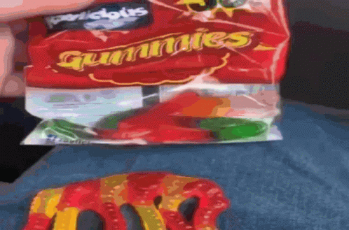 A Person Is Holding A Bag Of Gummies Next To A Gummy Worm GIF