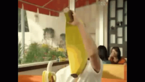 A Person Is Holding A Banana Over Their Head While Sitting At A Table . GIF