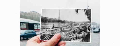 a person is holding a black and white photo of a pile of cars in front of the eiffel tower